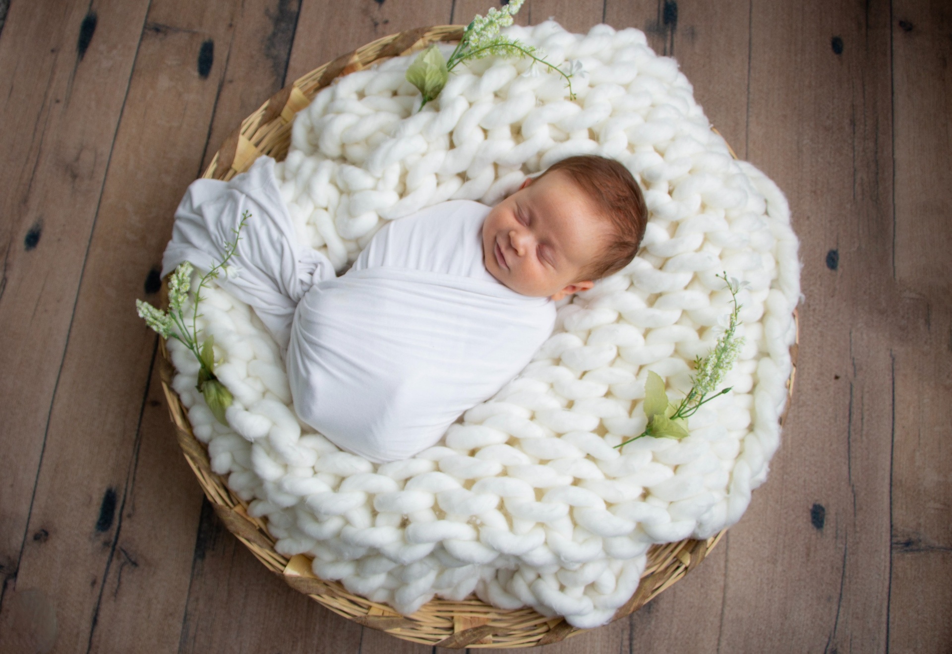 Newborn sleeping in a basket with a chunky knit blanket