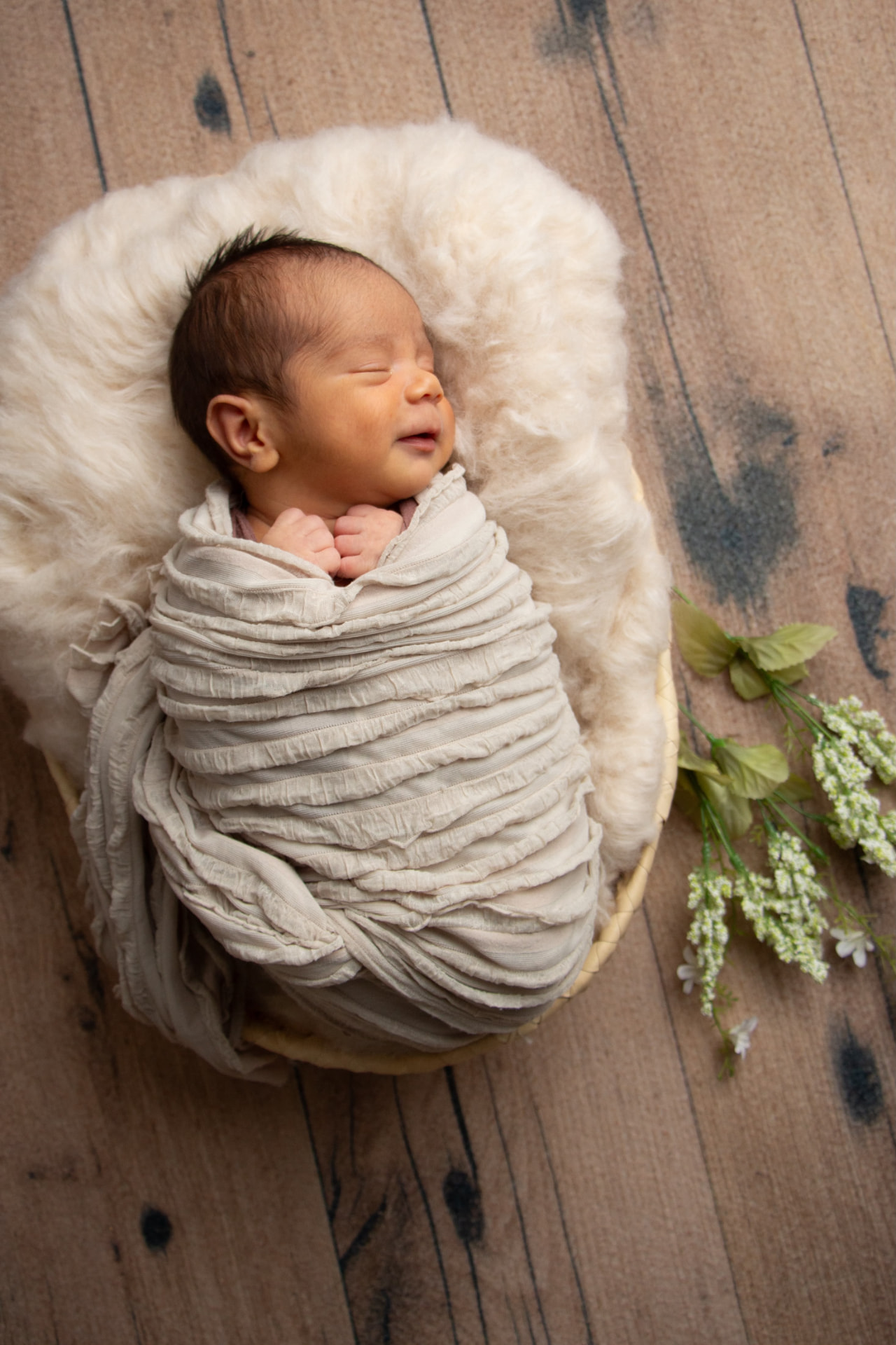 Newborn wrapped in soft cream fabric, resting peacefully in a cozy basket