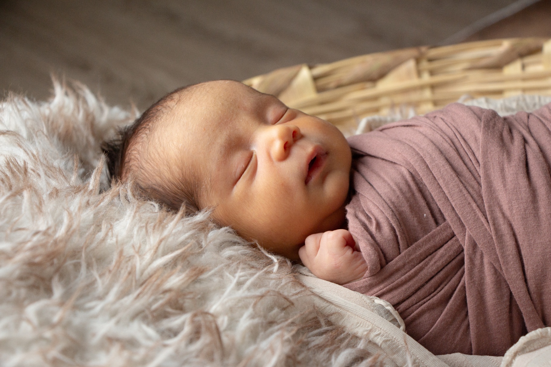 Newborn wrapped in a mauve blanket on a white fur rug