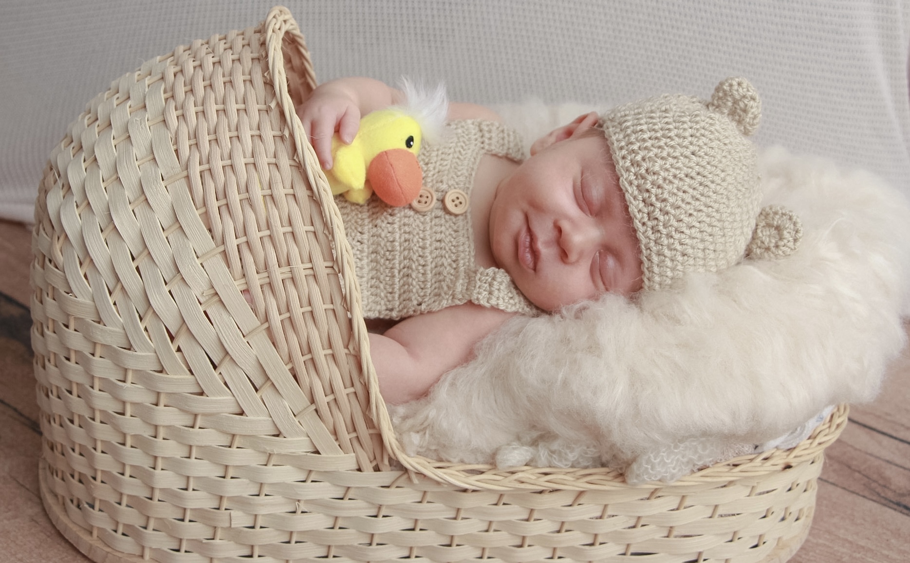 Newborn in a tan knit outfit with a yellow duckling toy